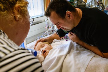 Emotionele vader aait over hoofd van kind in ziekenhuisbed na operatie
